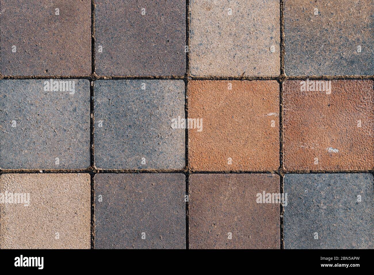 Superficie stagionata di pavimento rustico coperto con piastrelle quadrate di terracotta di varie sfumature di colore marrone e grigio Foto Stock
