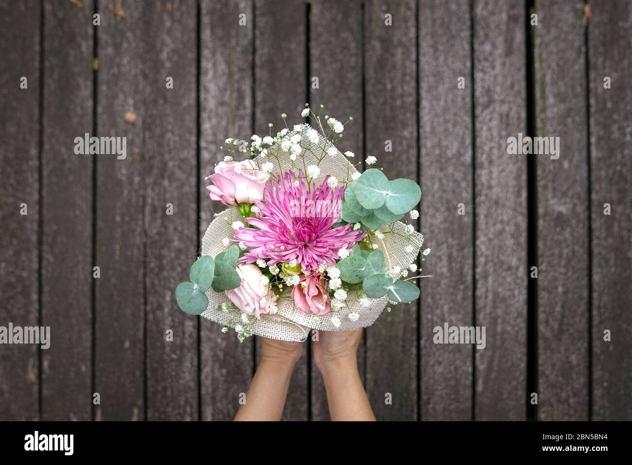 Donna che tiene mano bouquet di fiori. Legno scuro platks sfondo. Spazio di copia. Foto Stock