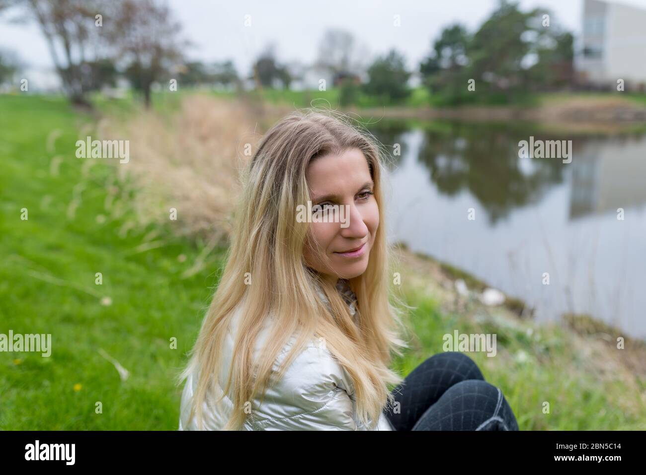 Donna/ragazza seduta su un'erba di fronte all'acqua di un lago Foto Stock