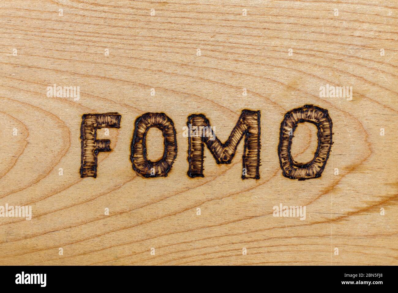 Abbreviazione FOMO - paura di perdere - bruciato da mano su superficie piana di legno Foto Stock