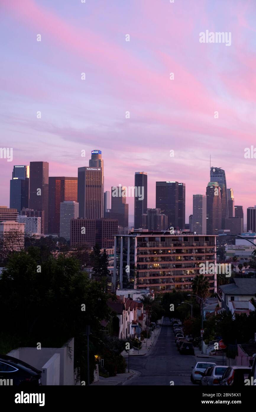 Guardando una strada verso lo skyline del centro di Los Angeles sotto un cielo rosa al tramonto Foto Stock