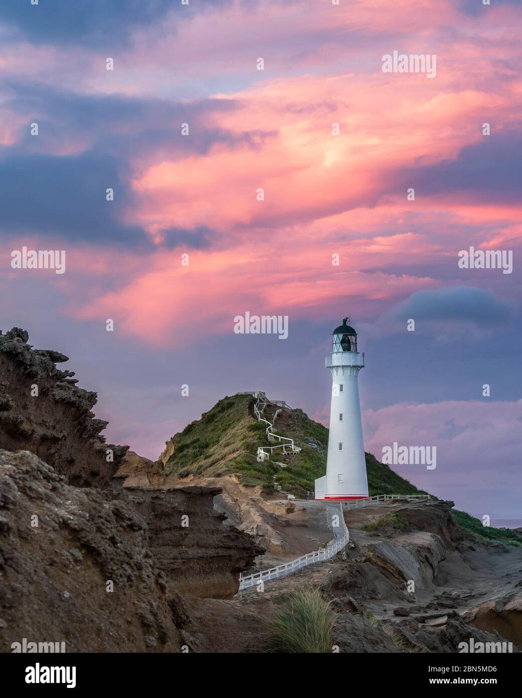 Faro nella luce della sera sotto un cielo rosa nuvoloso sulle scogliere a Castlepoint, Lavafels, Masterton, Wellington, Nuova Zelanda Foto Stock
