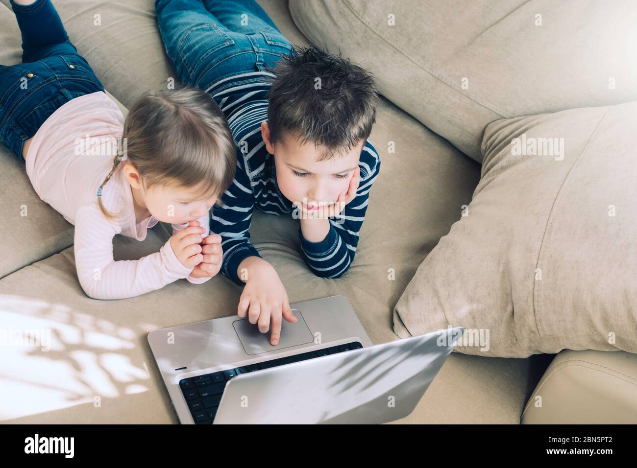 I bambini studiano a casa utilizzando lezioni online sul divano, guardando cartoni animati online. Quarantena a casa. Formazione a distanza, formazione online. Foto Stock