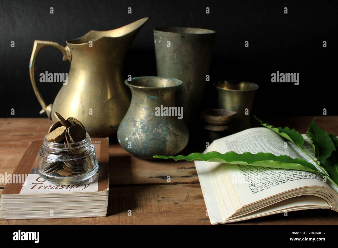 Vecchi utensili vintage con libro e monete di rupia indiana. Vecchi utensili in ottone metallico su pavimento in legno. Foto Stock
