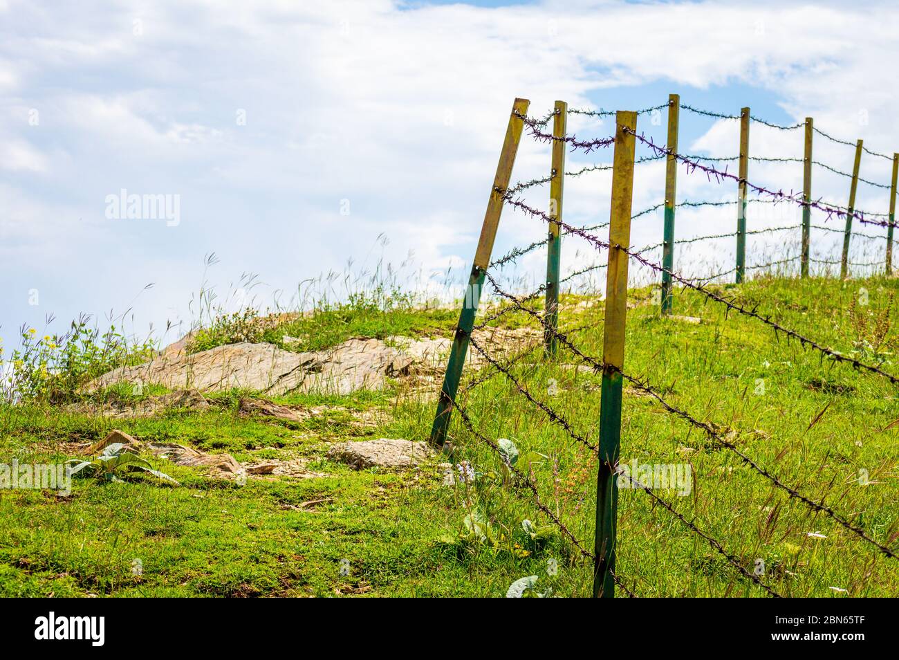 Una recinzione a catena in un prato aperto con cielo blu nuvoloso Foto Stock