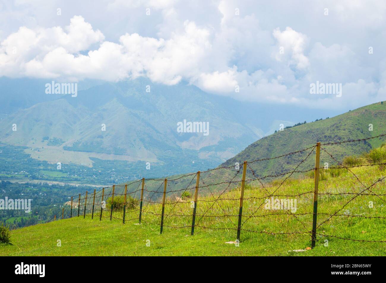 Una recinzione a catena in un prato aperto con cielo blu nuvoloso. Confine geografico. Recinzione per la fauna selvatica per tenere gli animali lontano Foto Stock