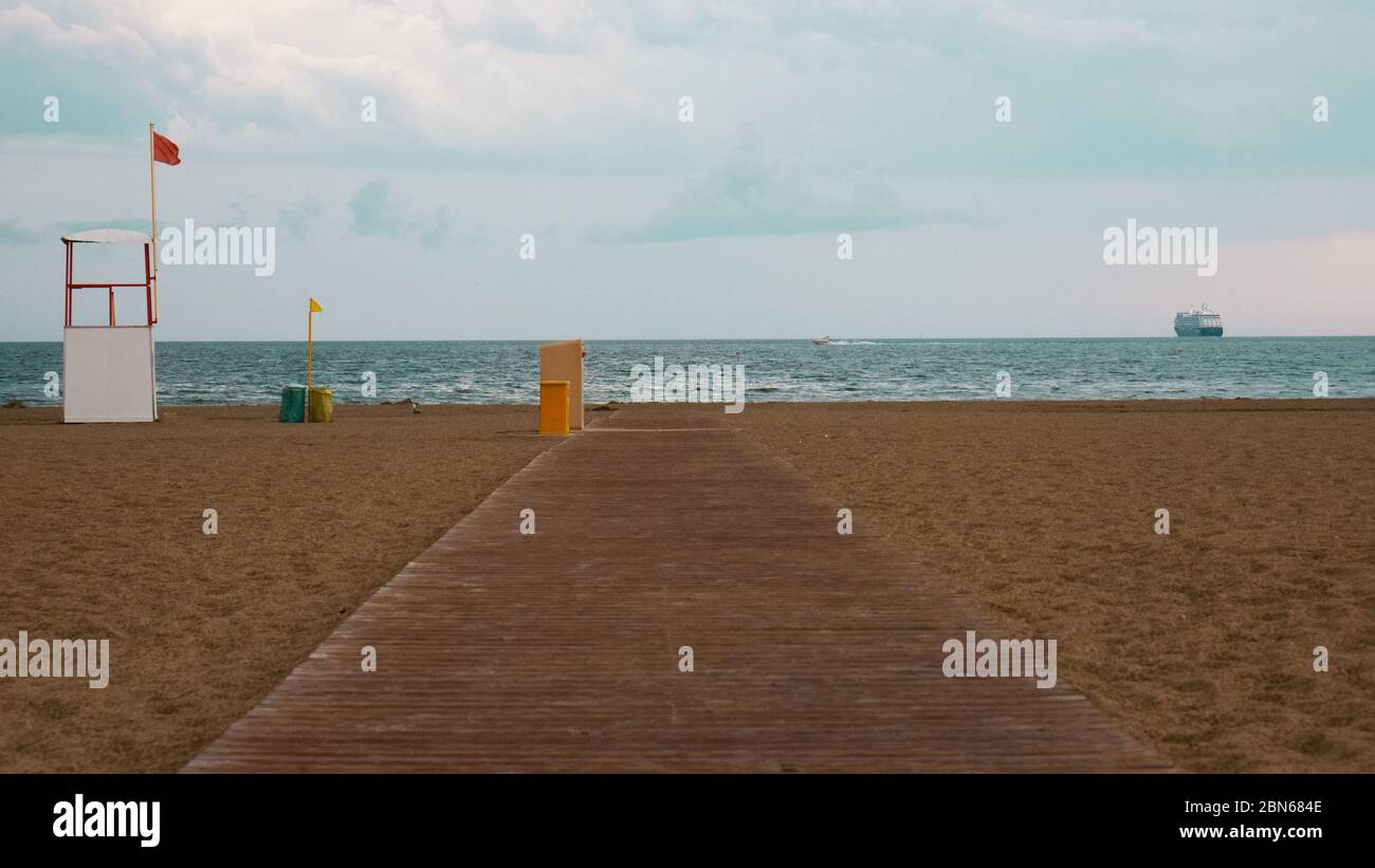 Spiaggia abbandonata con tavole di legno a causa della tempesta. Con un allarme rosso di pericolo. Sullo sfondo, una nave da crociera sta recedendo. Foto Stock