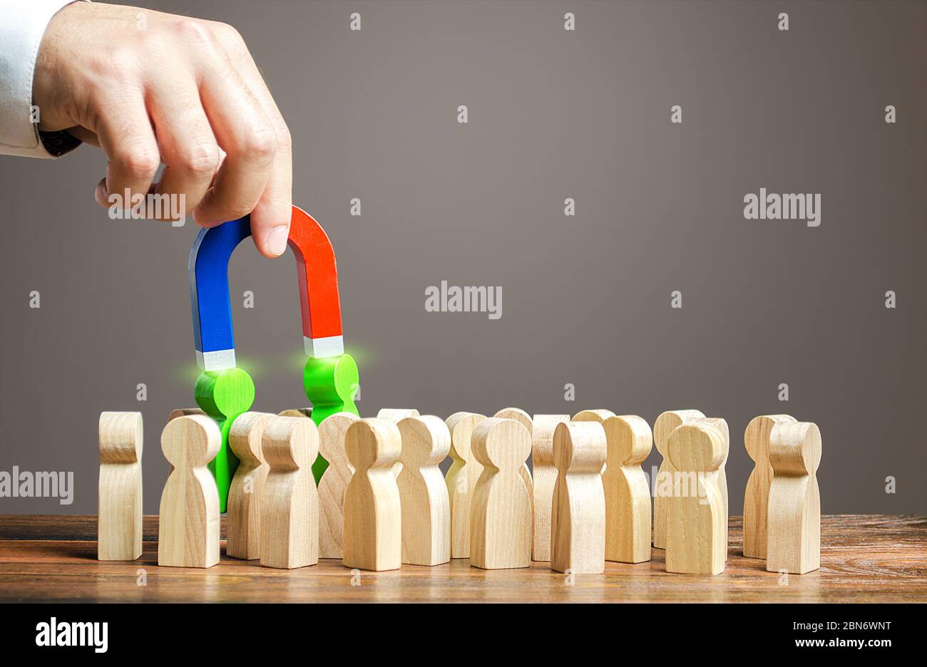 Una mano con un magnete tira fuori dalla folla le persone verdi. Reclutamento di nuovi lavoratori, cacciatori di testa. Cerca lavoratori di talento. Scegliere un candidato per il lavoro, c Foto Stock