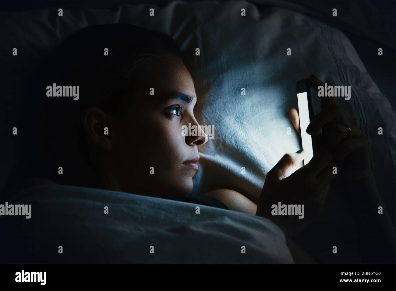 Giovane womanl bello a letto utilizzando il telefono cellulare a tarda notte in camera da letto buio, Internet dipendenza concetto Foto Stock