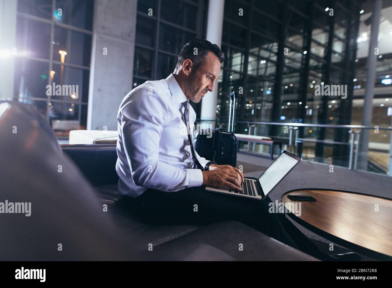 Uomo d'affari che aspetta all'aeroporto con il computer portatile. Uomo in abbigliamento formale seduto nella zona di partenza dell'aeroporto utilizzando il suo laptop. Foto Stock