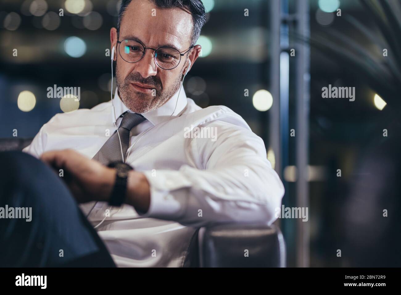 Uomo d'affari che aspetta all'aeroporto l'orario di controllo. Uomo in formalwear seduto alla partenza dell'aeroporto guardando il suo orologio da polso. Foto Stock