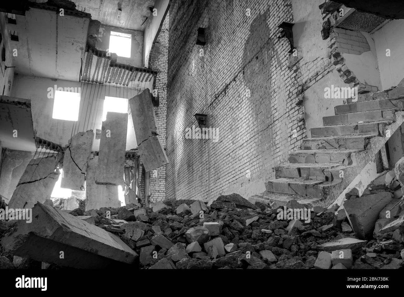 Immagine in bianco e nero. Edificio in cemento distrutto all'interno con un mucchio di detriti di costruzione in primo piano e grandi lastre di cemento appese a reba Foto Stock