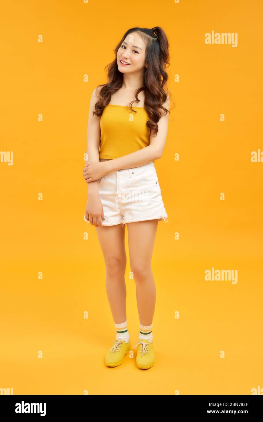 Giovane bella donna asiatica ridendo timidamente e allegro, con un atteggiamento amichevole e positivo ma insicuro contro il muro giallo Foto Stock