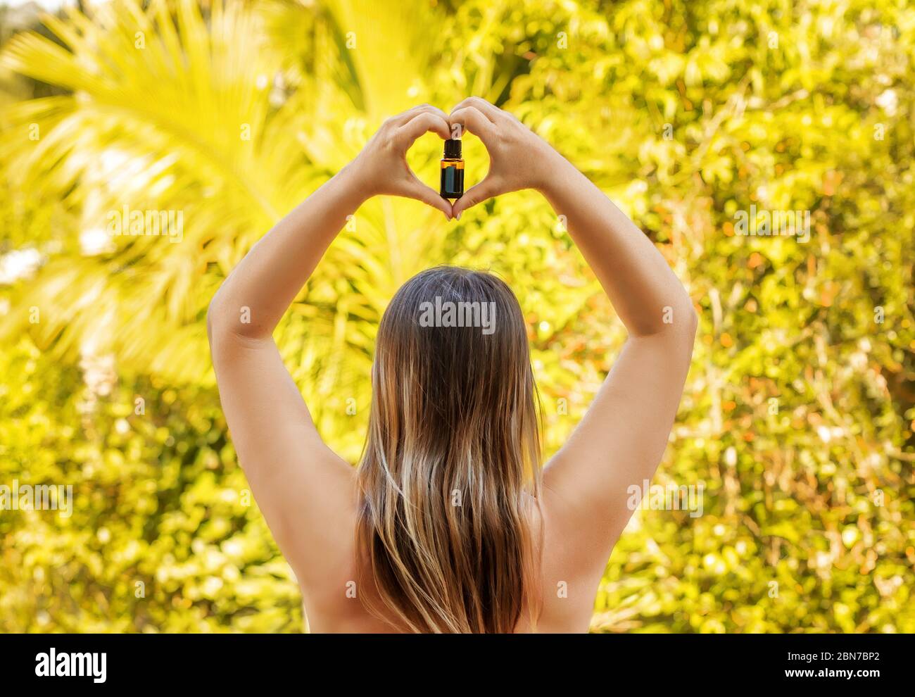 Donna tenere in mano la bottiglia di olio essenziale su sfondo giallo naturale, vista dal retro. Foto Stock