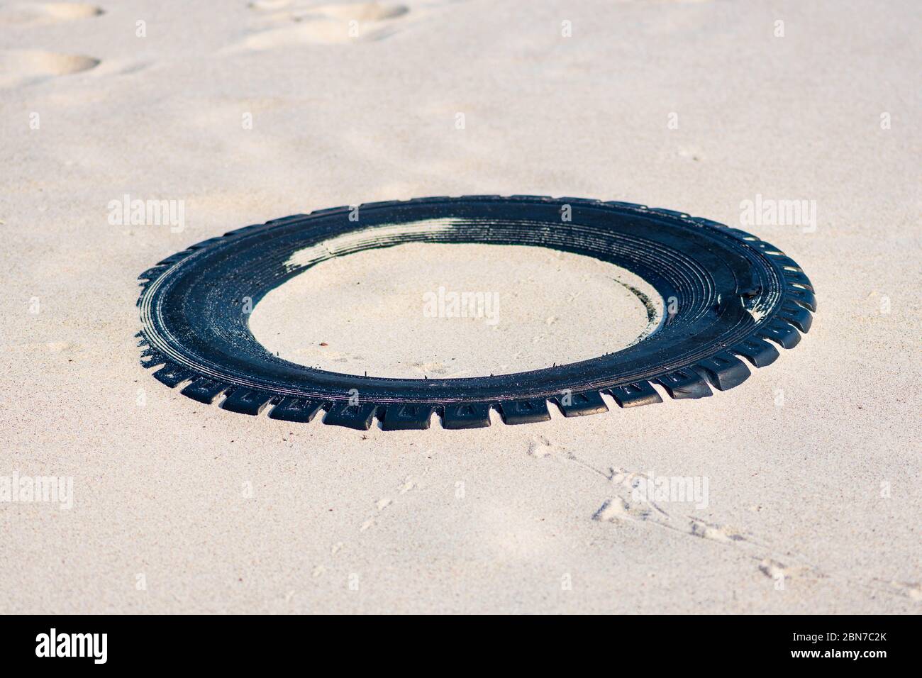 Grande pneumatico nero in gomma lasciato su una spiaggia sabbiosa, ambiente di inquinamento concetto Foto Stock