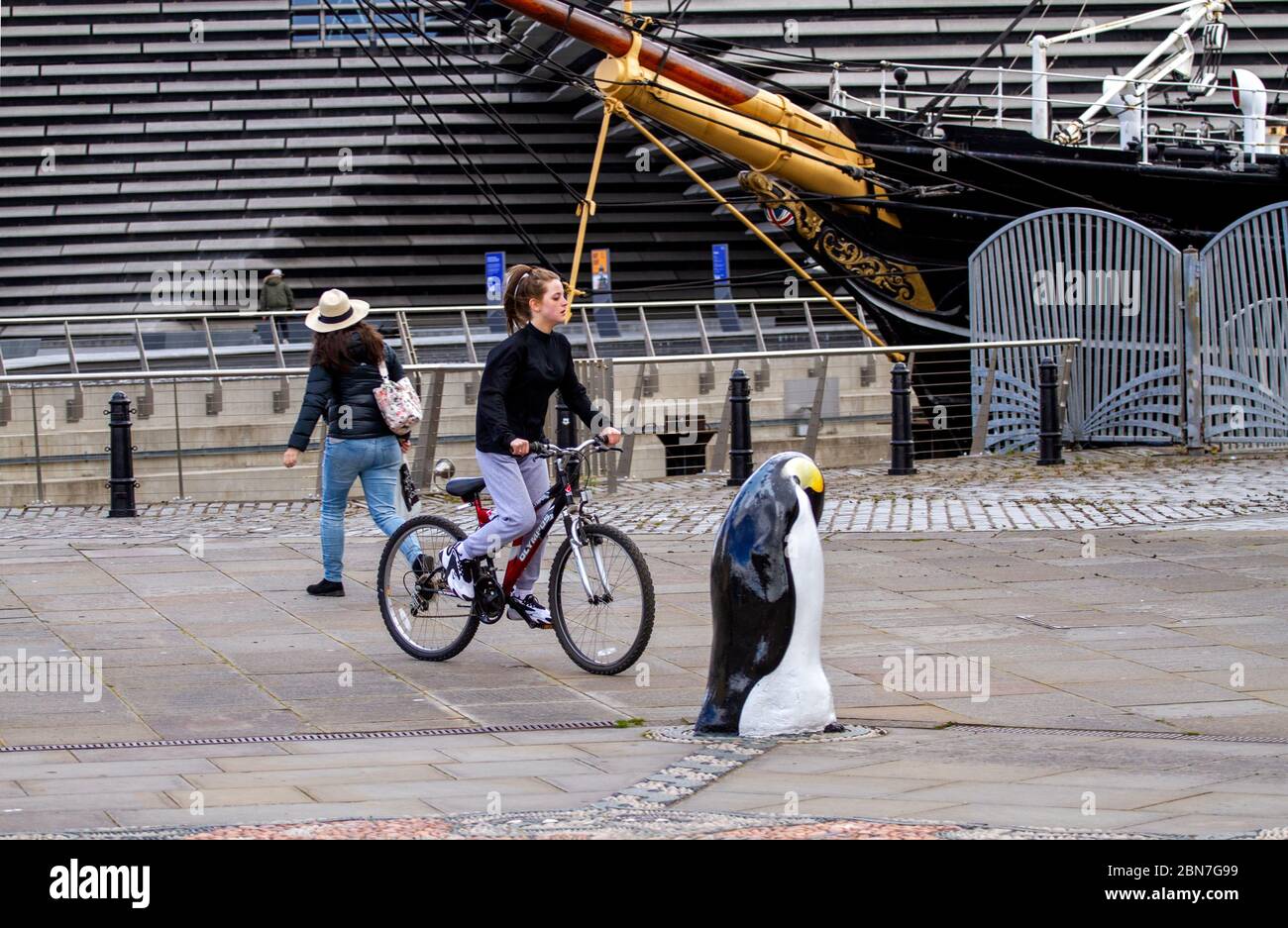 Dundee, Tayside, Scozia, Regno Unito. 13 maggio 2020. Tempo: Nuvoloso con alcuni intervalli soleggiati attraverso Tayside in Scozia con temperatura massima 14°C. Il primo Ministro Nicola Sturgeon ha annunciato nuove indicazioni che raccomandano al popolo scozzese di rendere obbligatorio indossare maschere in pubblico. Nonostante le normative sulla maschera facciale, i residenti locali si allenano alla luce lungo il lungomare di Dundee. Una giovane ciclista femminile ha una giornata fuori in bicicletta la sua bicicletta Olympus lungo Discovery Point accanto al V&A Design Museum e la nave RRS Discovery. Credit: Dundee Photographics/Alamy Live News Foto Stock