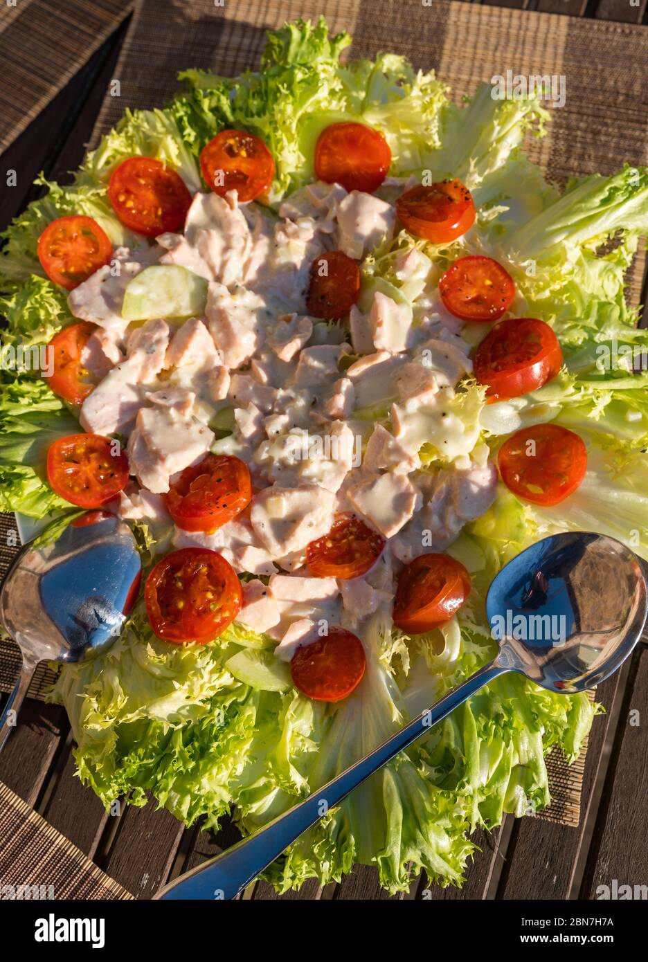 Primo piano di insalata estiva servita all'aperto con lattuga alla Frisée, pomodori ciliegini e salmone in maionese Foto Stock
