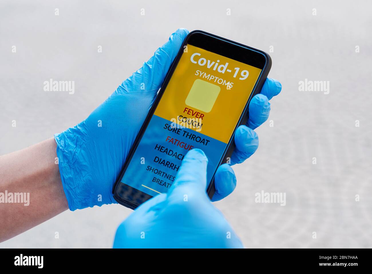 primo piano di un giovane uomo caucasico sulla strada, indossando guanti blu in lattice, controllando alcuni dei sintomi del covid-19 in una app simulata nella sua sma Foto Stock
