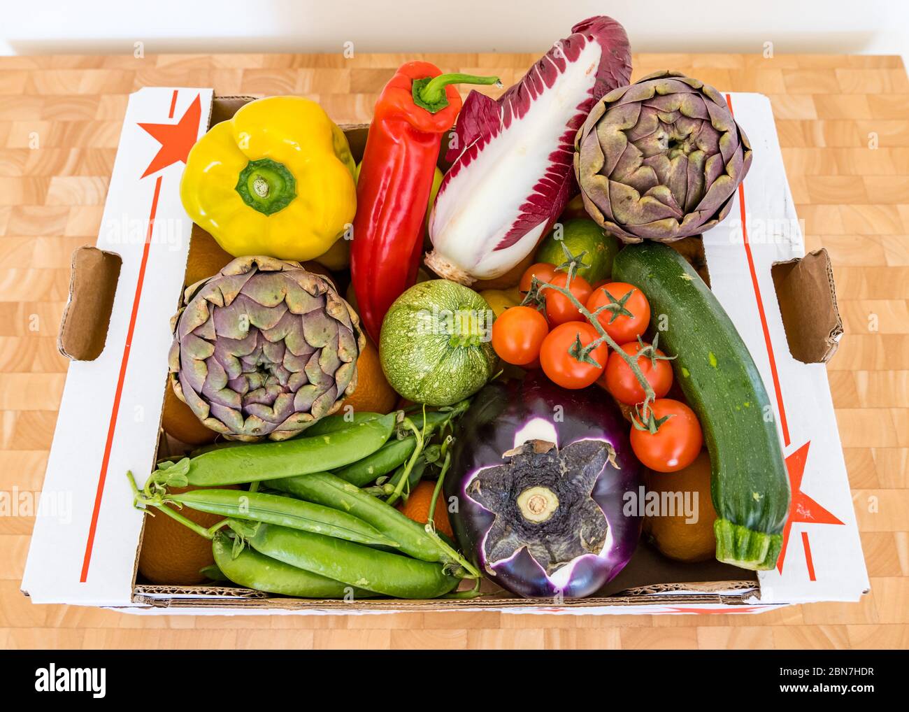 Scatola di consegna verdure con peperoni, indivia, melanzane, carciofi, cialde di piselli e pomodori ciliegini Foto Stock