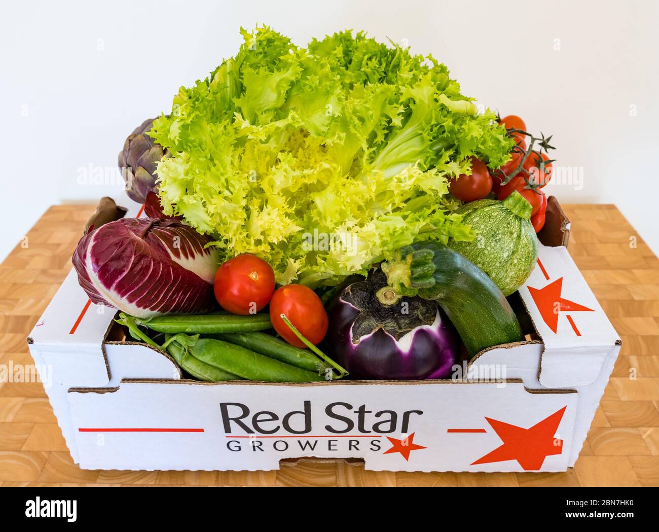 Scatola di consegna verdure con lattuga Frisée, indivia, melanzane, carciofi, zucchine, cialde di piselli e pomodori ciliegini Foto Stock