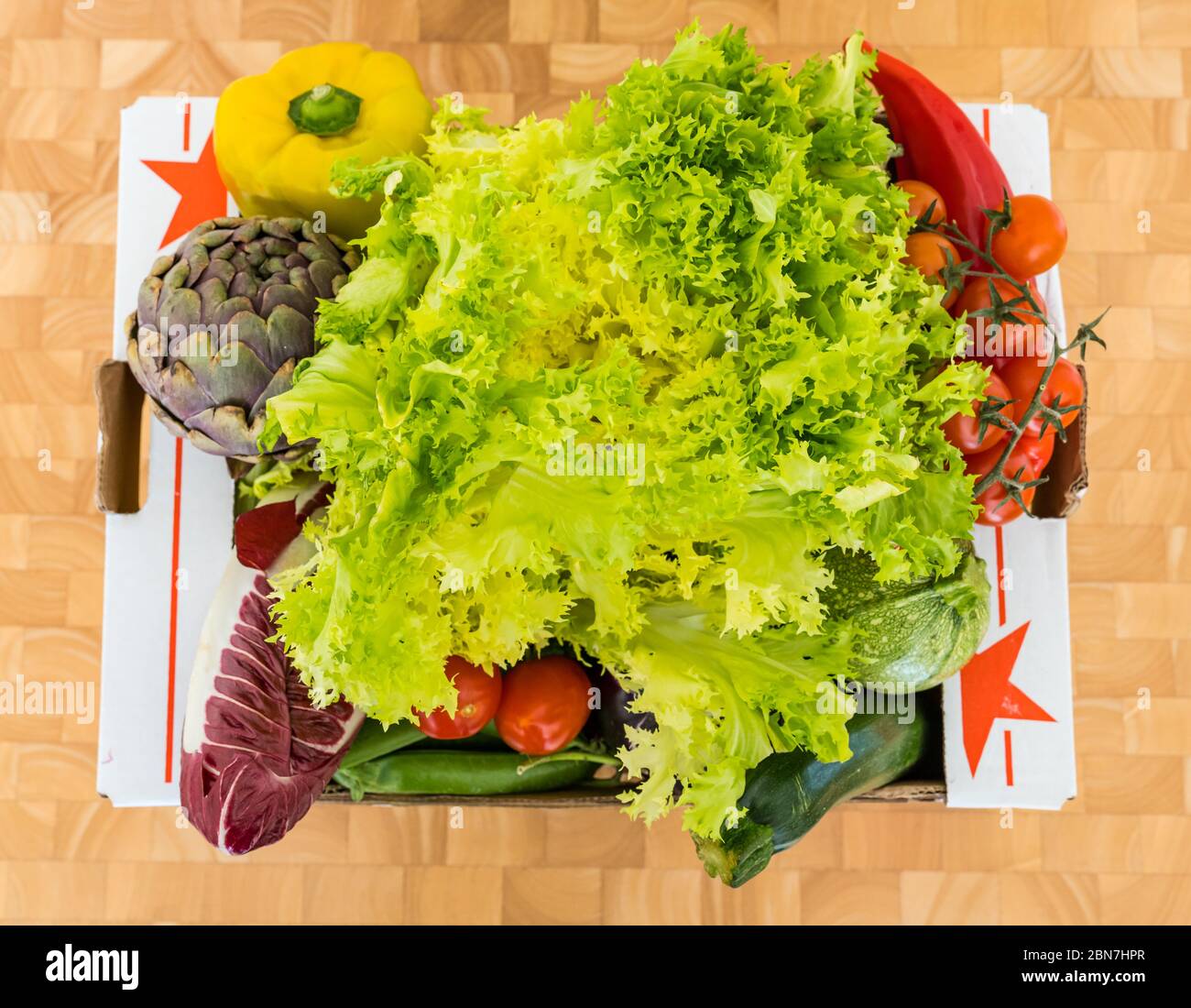 Scatola di consegna verdure con lattuga Frisée, peperoni, indivia, melanzane, carciofi, zucchine, cialde di piselli e pomodori ciliegini Foto Stock