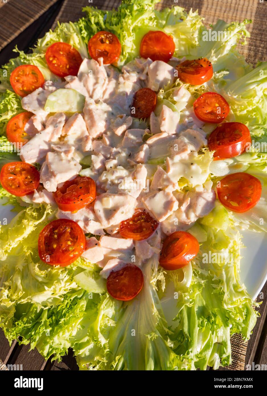 Primo piano di insalata estiva servita all'aperto con lattuga alla Frisée, pomodori ciliegini e salmone in maionese Foto Stock