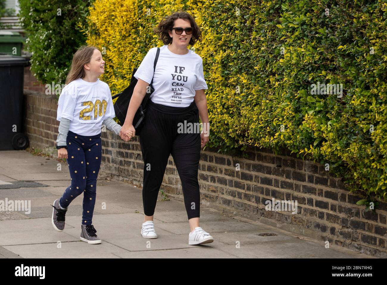 Fiona e sua figlia Lola, di Londra, indossano le T-shirt che includono lo slogan: "Se potete leggere questo, siete troppo vicini per COVID" che sono stati lanciati dalla società globale di trasformazione del marchio FutureBrand come un'iniziativa no-profit per contribuire a rafforzare le linee guida chiave di distanza sociale come la nazione emerge dal blocco pandemico del coronavirus. Foto Stock