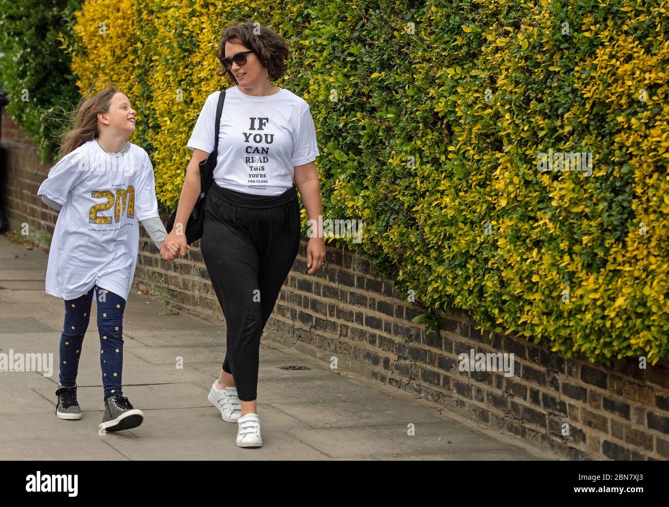 Fiona e sua figlia Lola, di Londra, indossano le T-shirt che includono lo slogan: "Se potete leggere questo, siete troppo vicini per COVID" che sono stati lanciati dalla società globale di trasformazione del marchio FutureBrand come un'iniziativa no-profit per contribuire a rafforzare le linee guida chiave di distanza sociale come la nazione emerge dal blocco pandemico del coronavirus. Foto Stock