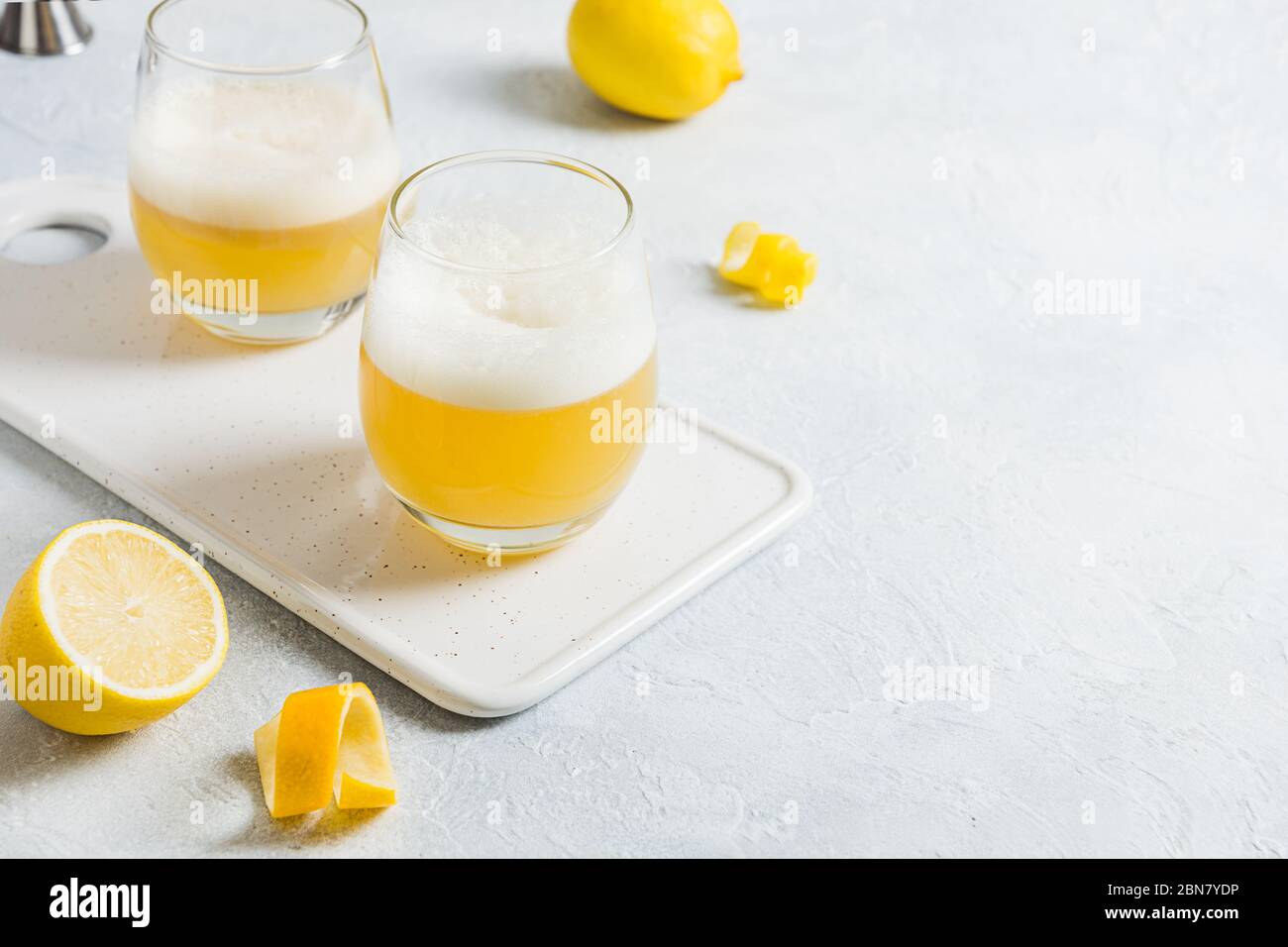 Due cocktail acini con ingredienti, succo di limone, sciroppo di zucchero e albume d'uovo su un tavolo bianco. Orientamento orizzontale. Primo piano. Foto Stock