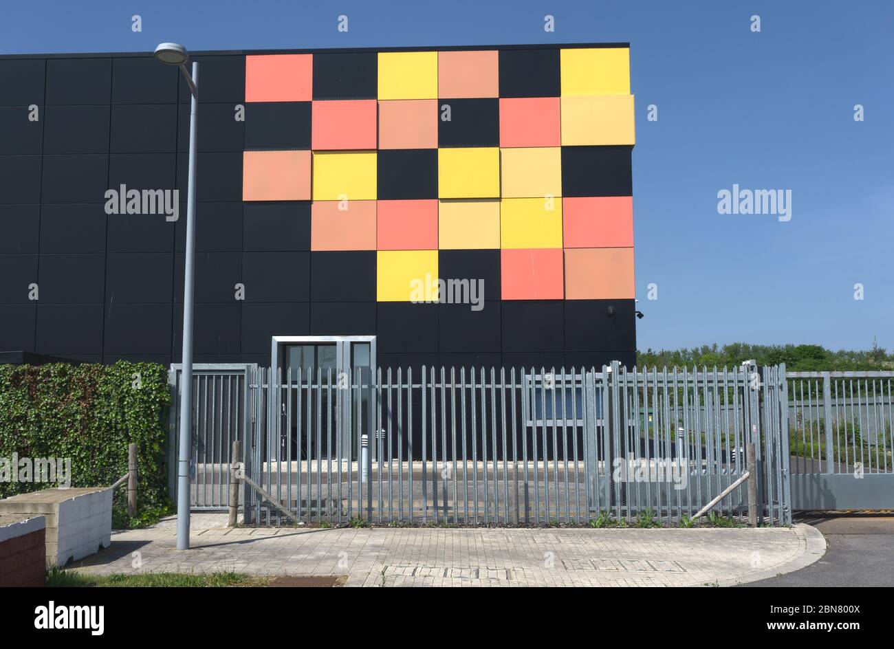 Edificio cubico nero opaco con piastrelle gialle e rosse in un angolo come design grafico dietro le ringhiere di sicurezza in metallo, data center cielo blu intenso Foto Stock