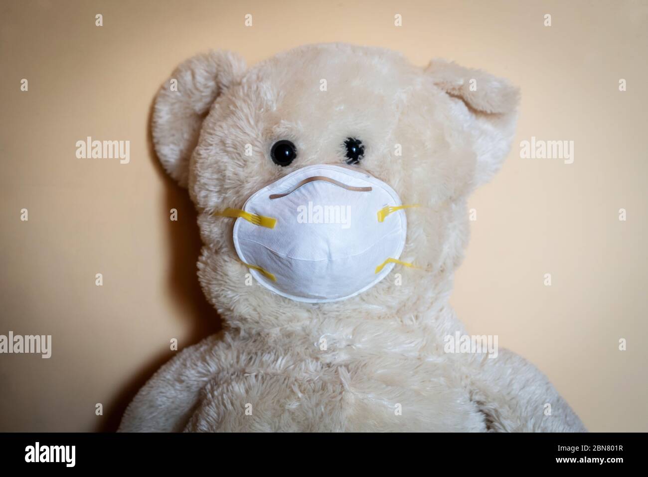 Orsacchiotto con maschera medica protettiva su sfondo giallo. Concetto di trattamento pediatrico, igiene, protezione da epidemie e virus per i pazienti pediatrici. Foto Stock