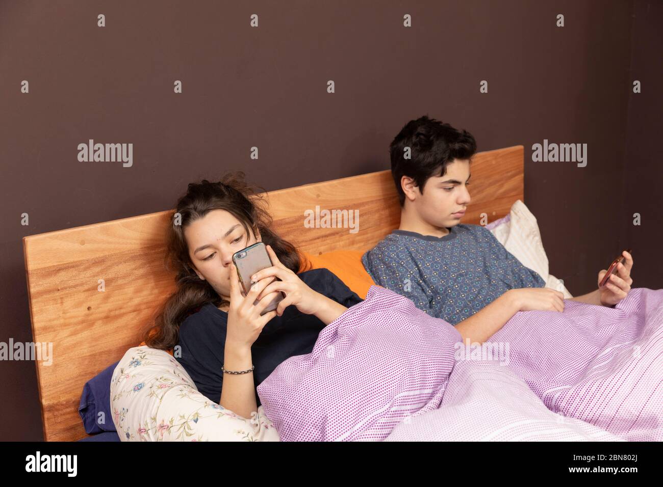 Una ragazza e un ragazzo insieme nel letto matrimoniale. Anche se sono insieme, tutti sono soli con il suo telefono. Foto Stock