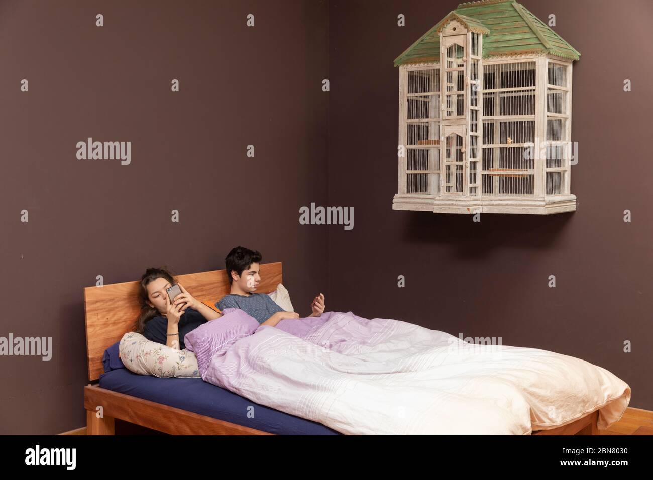 Una ragazza e un ragazzo insieme nel letto matrimoniale. Anche se sono insieme, tutti sono soli con il suo telefono. Foto Stock