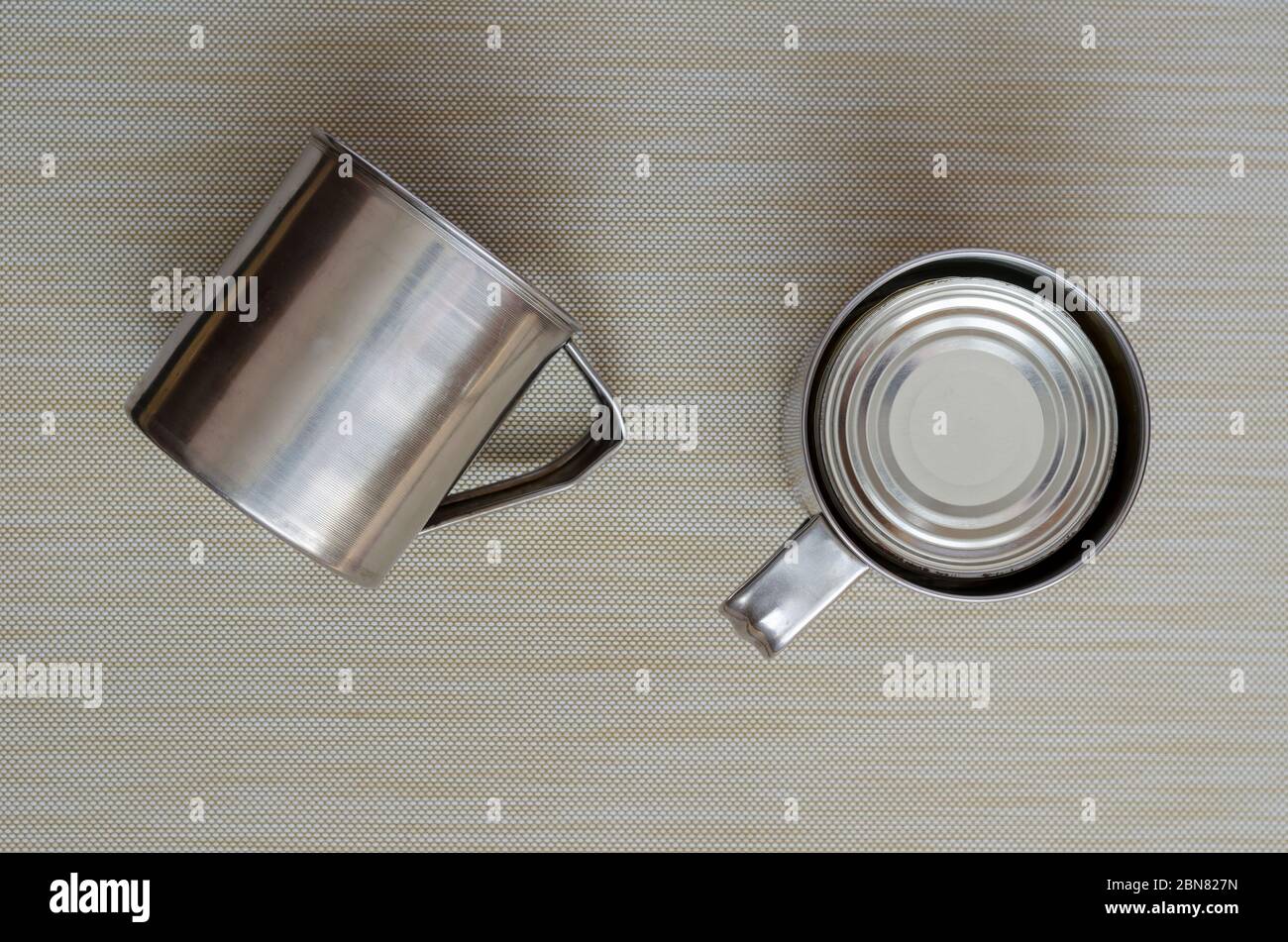 Due tazze di metallo e un lattino. Stufati chiusi in scatola e tazze in acciaio inox. Escursioni e viaggi. Vista dall'alto. Primo piano. Foto Stock