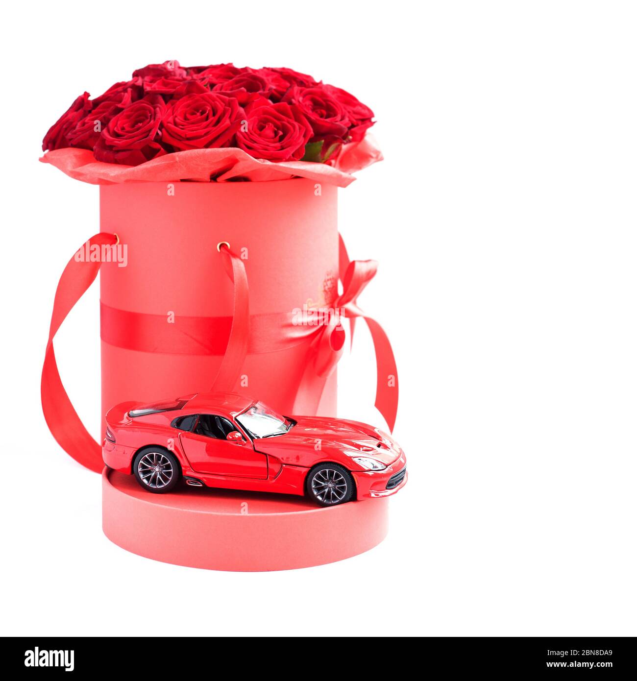 Mosca, Russia - 6 maggio 2020: Auto moderna giocattolo rosso contro rose rosse di lusso in scatola cappello di carta su sfondo bianco. Regalo romantico per donna Foto Stock
