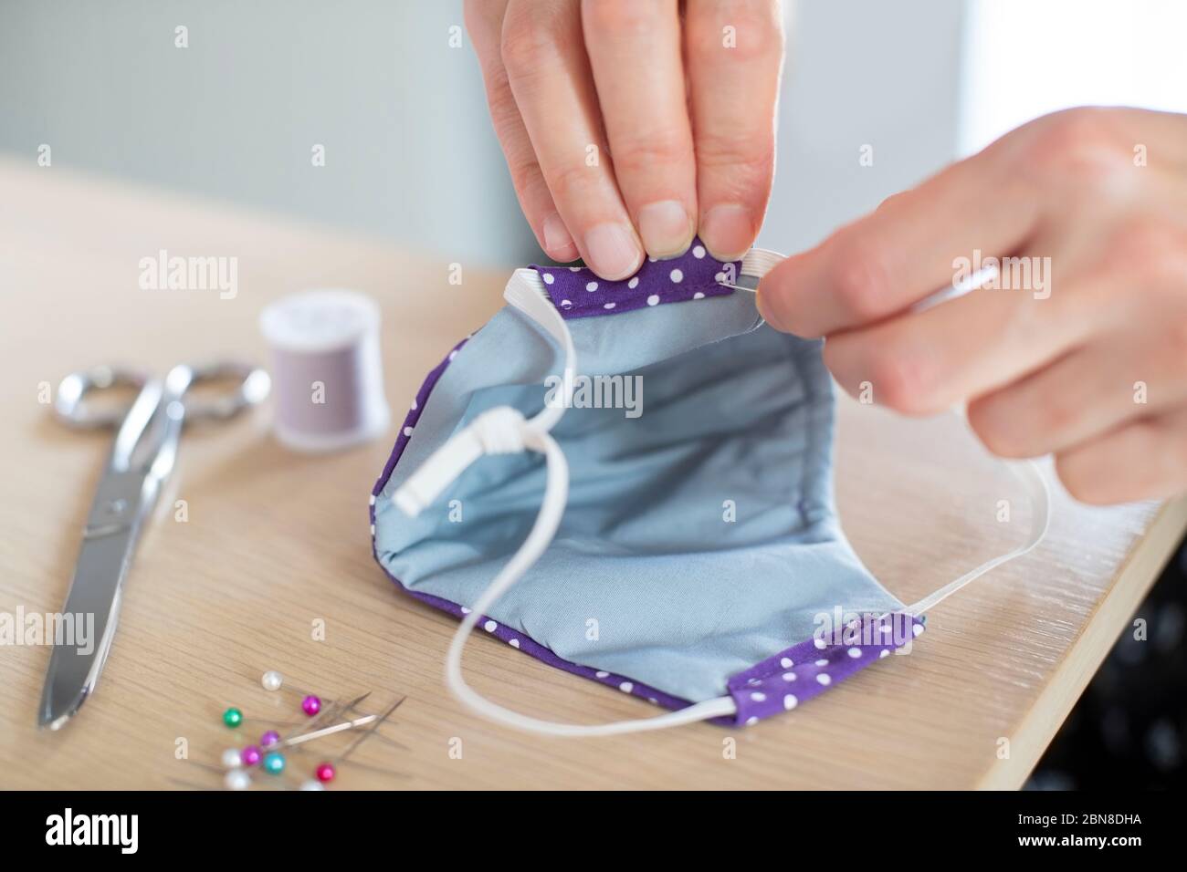 Primo piano della persona cucire mano fatto PPE maschera facciale durante Covid-19 scoppio Foto Stock