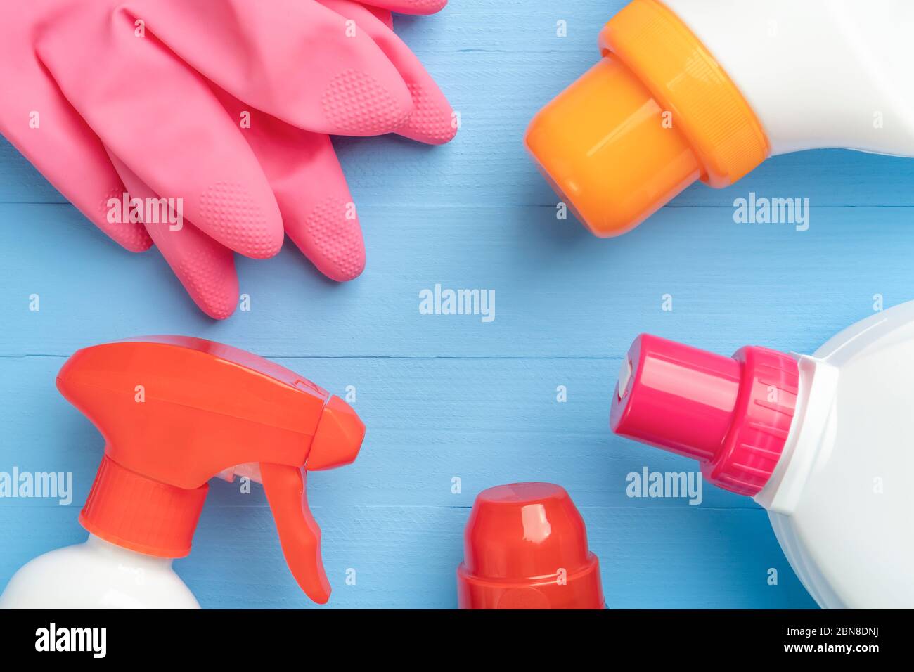 Set di prodotti per la pulizia in bottiglie di plastica lucida e uno straccio giallo con guanti di protezione rosa per il lavaggio domestico da vicino su fondo di legno Foto Stock