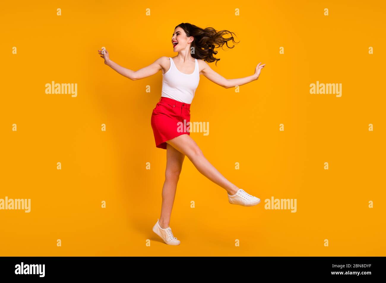 Foto profilo full size di divertente ragazza alzate le mani gamba gioire estate weekend caldo brezza soffiando indossare bianco serbatoio-top gonna scarpe rosse Foto Stock