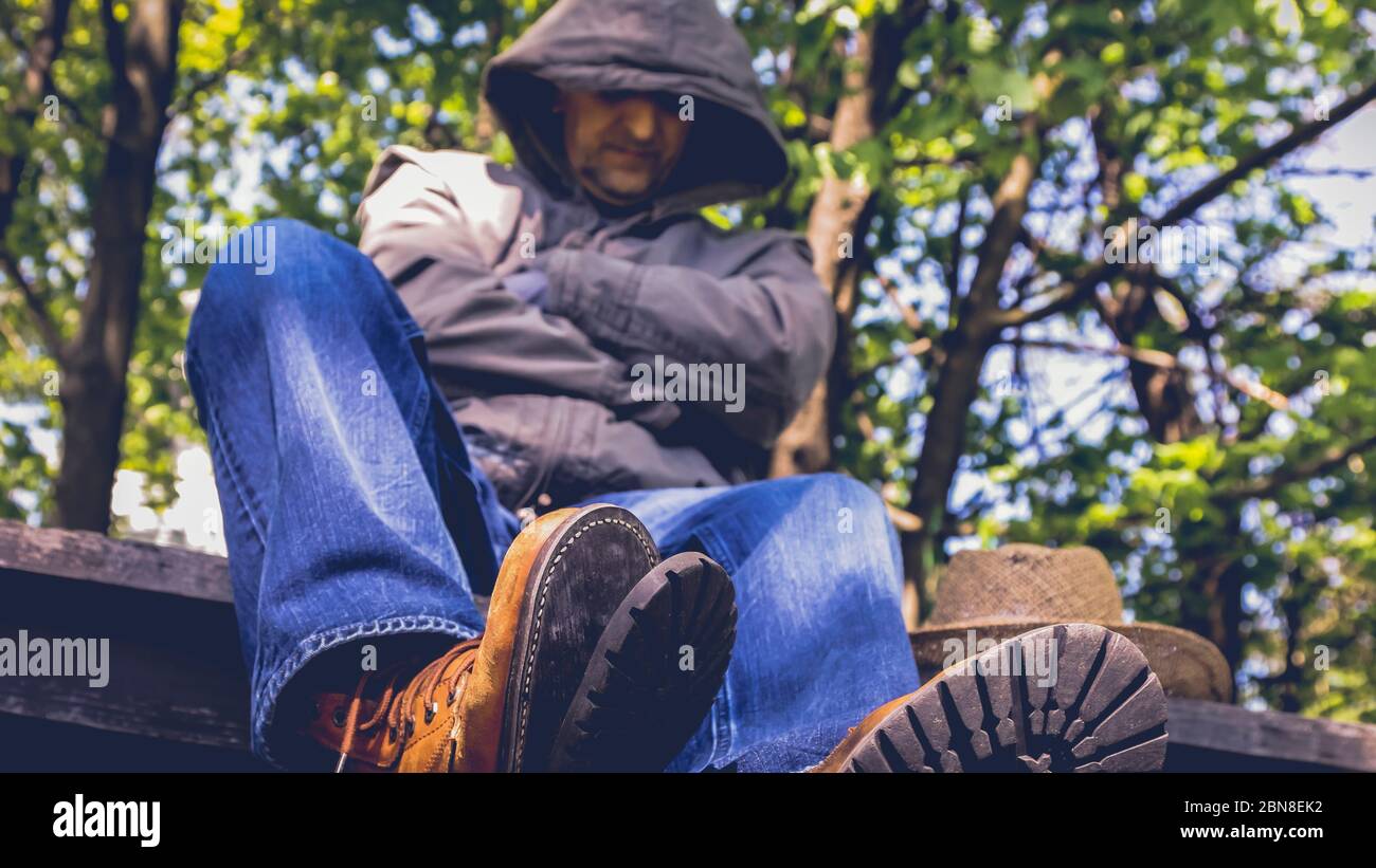 Escursionista seduto sul tavolo con alberi dietro e una vista di stivali rotti di fronte Foto Stock