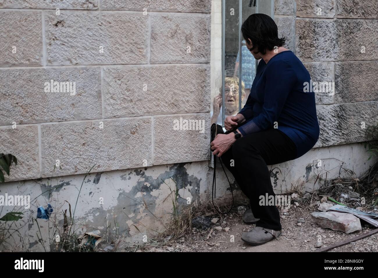 Gerusalemme, Israele. 13 maggio 2020. Le famiglie trascorrono il tempo con gli anziani in una casa di vita assistita, sotto severe restrizioni sociali di allontanamento che vietano i visitatori, attraverso una zona allestita in un vicolo posteriore per questo scopo. In linea con la direttiva del Ministero della Sanità ‘no kissing, no hugging, no tocing' questa disposizione garantisce che la distanza di due metri possa essere mantenuta o l'interazione attraverso una partizione trasparente. Credit: NIR Alon/Alamy Live News Foto Stock