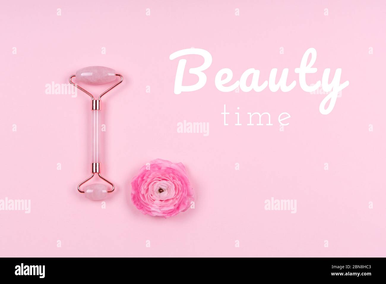 Rullo di Giada con fiore di ranunculus su goccia rosa con la formulazione del tempo di bellezza. Tempo di bellezza, cura di se stessi, giornale di bellezza, concetto di rivista femminile Foto Stock