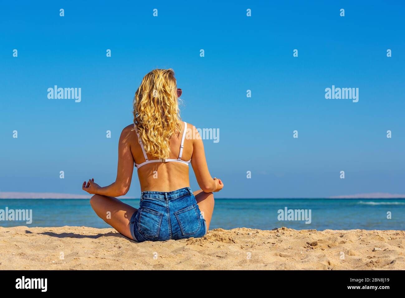 Giovane bionda caucasica con capelli lunghi medita sulla spiaggia egiziana Foto Stock