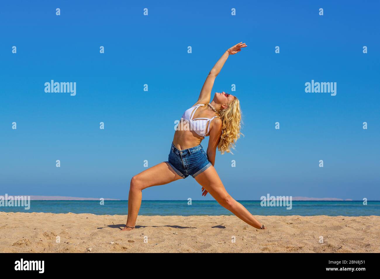 Giovane bionda caucasica donna di formazione yoga sulla spiaggia vicino al mare Foto Stock