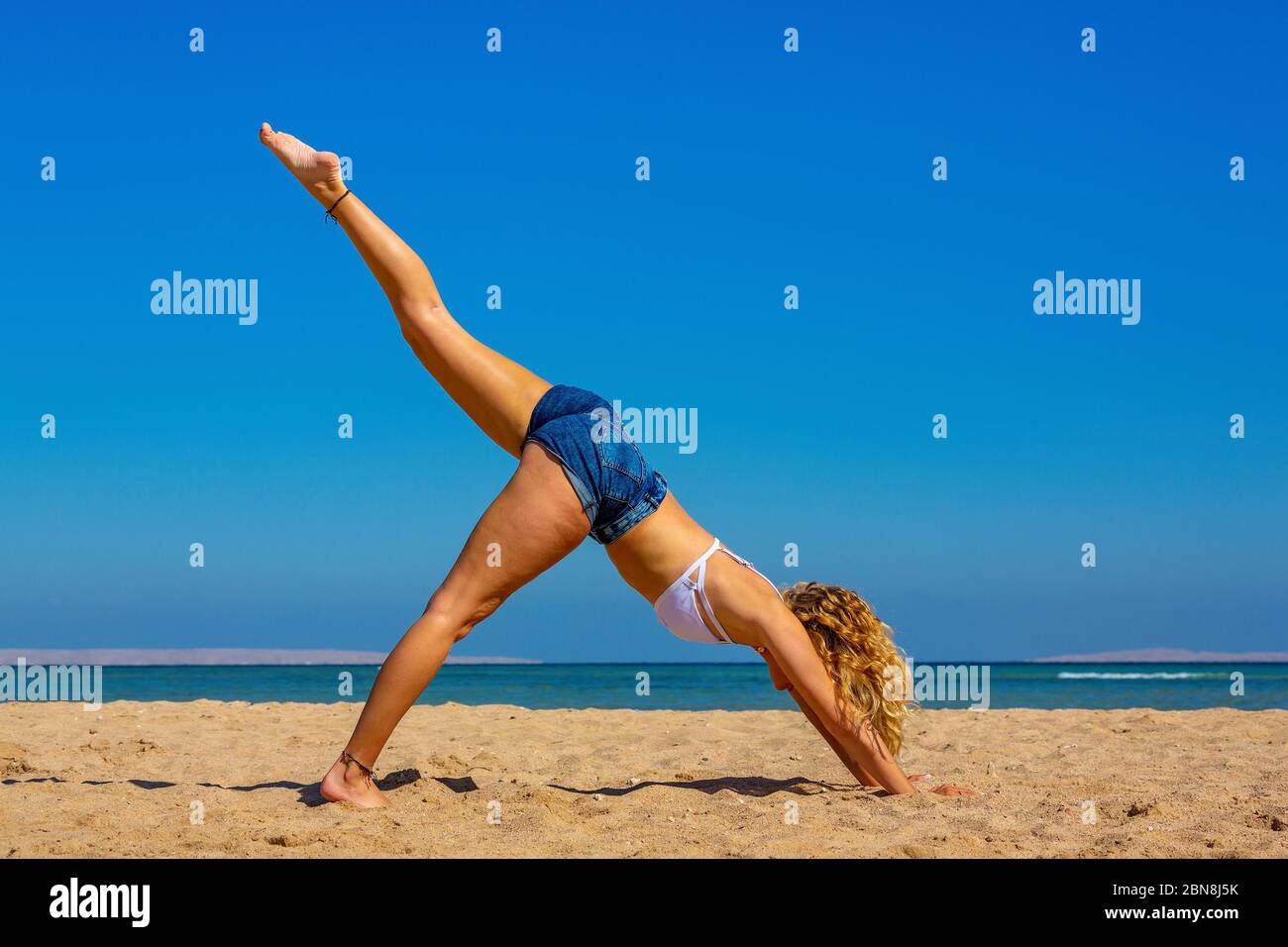 Giovane bionda in posizione yoga diritta sulla spiaggia egiziana Foto Stock
