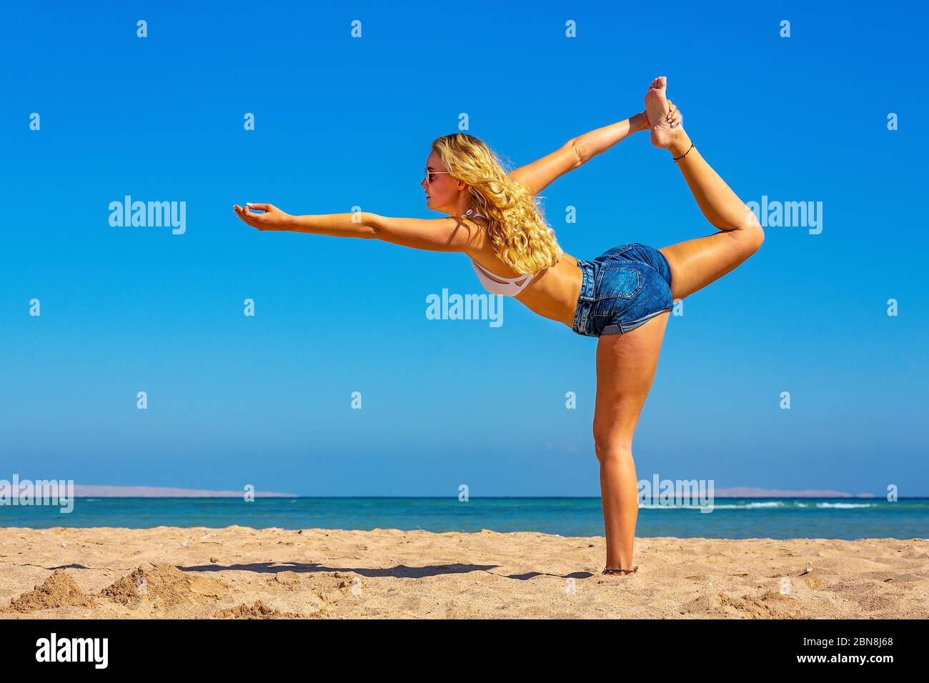 Giovane bionda donna in posa yoga sulla spiaggia egiziana Foto Stock