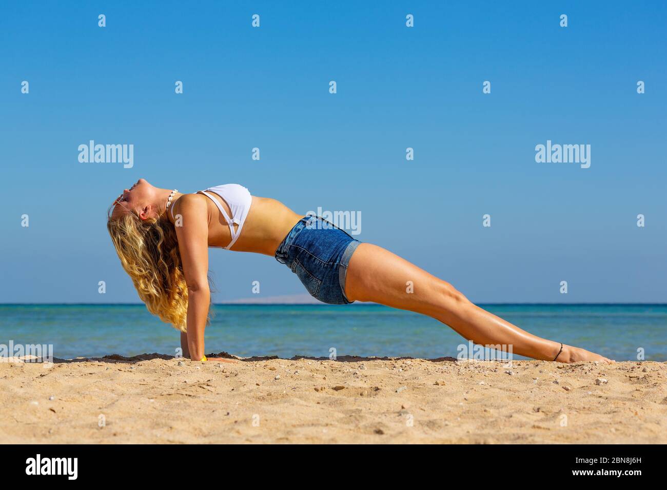 Giovane caucasica che pianse indietro sulla spiaggia per l'esercizio di yoga Foto Stock