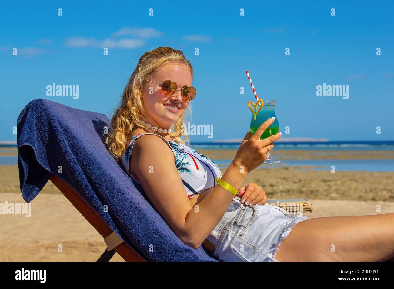 Giovane caucasica che beve un cocktail alcolico sul letto della spiaggia Foto Stock