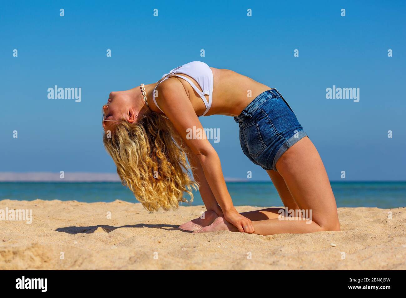 Giovane caucasica in posizione di curva posteriore sulla spiaggia egiziana vicino al mare blu Foto Stock