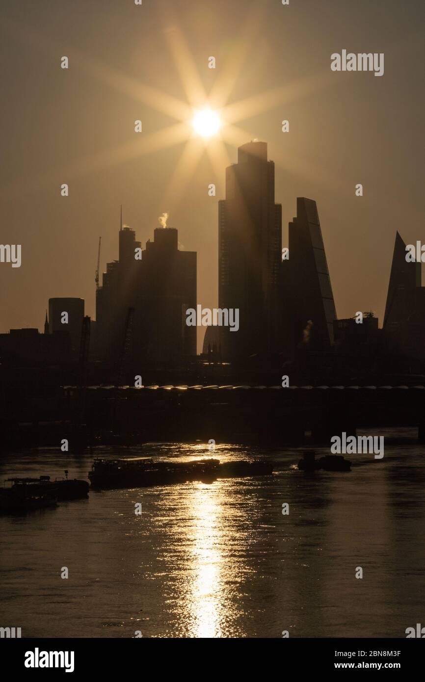 Sunrise a Londra crea una silhouette della City di Londra con il Tamigi e le barche fluviali in primo piano. Foto Stock