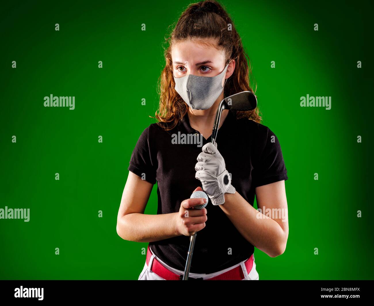 Primo piano di ragazza giocatore di golf con maschera protettiva attende il suo turno per fare il suo miglior colpo, isolato su sfondo verde Foto Stock